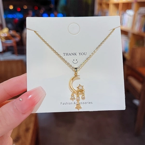 Close-up of golden crescent moon and stars pendant necklace with white zircons on card