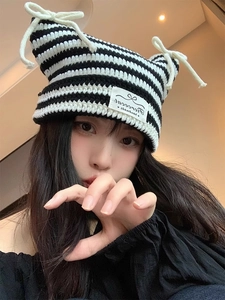 Detail of knitted cat ear beanie with black and white stripes and ribbon bow accents
