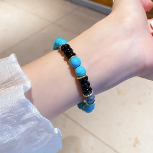 Close-up of beaded bracelet with turquoise, black agate, and gold wavy spacers on wrist