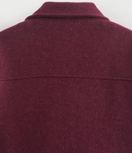 Détail du col et des coutures d'épaule d'une veste en laine bordeaux sur fond uni