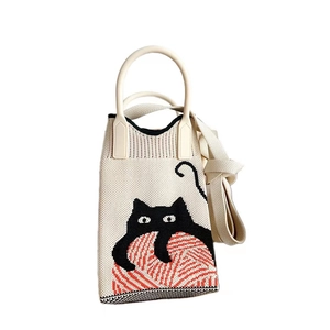 Detail of beige knitted phone bag featuring a cute black cat and red yarn pattern