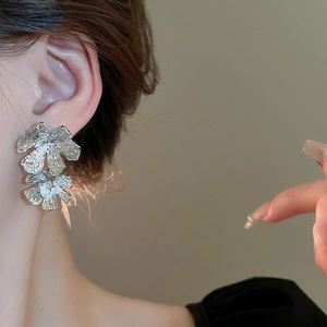 Close-up of elegant silver textured flower stud earrings worn by a model in soft lighting
