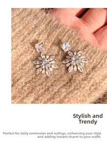 Macro shot of silver snowflake drop earrings with sparkling zircon on a warm knit background
