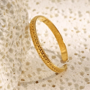 Macro shot of gold-plated stainless steel ring with textured dot pattern on white coral