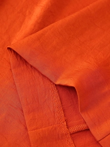 Close-up of orange satin fabric showing detailed overlock stitching and woven texture