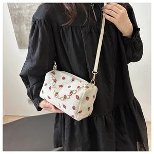 Close-up of a white corduroy cylinder bag with strawberry prints and a gold flower chain