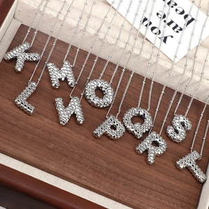 Detailed shot of silver initial pendant necklaces K to T on wooden tray and beige cloth