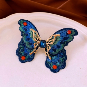 Detailed close-up of butterfly embroidery pin with blue crystal on a ceramic tray