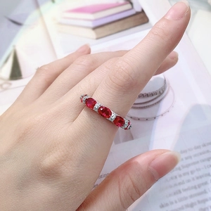 Close-up of five oval red rubies set in a diamond paved band worn on a finger