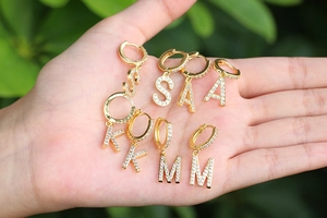 Macro shot of gold letter earrings with zircons held in hand with garden background