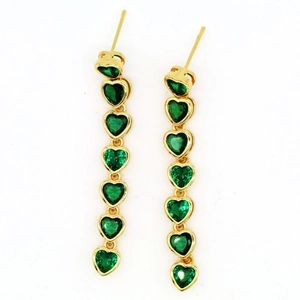 Primer plano de pendientes largos dorados con gemas verdes en forma de corazón