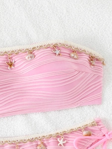 Detailed close-up of pink bikini fabric with sea shell charms and woven lace trim