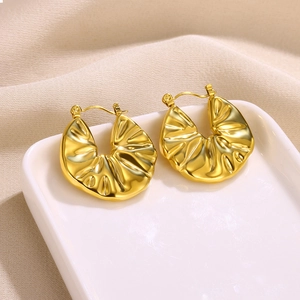 Close-up of golden petal earrings with pleated texture on white ceramic tray