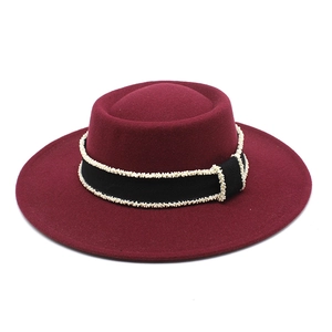 Detail of wine red wool felt fedora featuring a black ribbon and white pearl bead trim