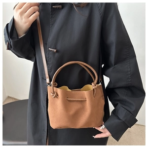 Detail of a brown suede tote bag with fixed arch handles and knot accents on black coat