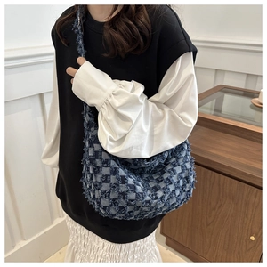 Detail of blue denim shoulder bag featuring woven lattice pattern and frayed fringe edges