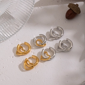 Minimalist heart-shaped hoop earrings in gold and silver finishes on a textured white surface