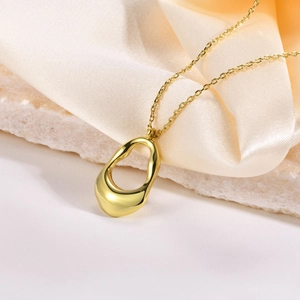 Detail of irregular hollow gold pendant on white stone and beige silk fabric background