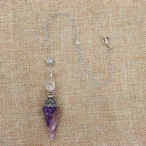 Detailed view of amethyst hex crystal pendulum with silver chain on rustic linen cloth