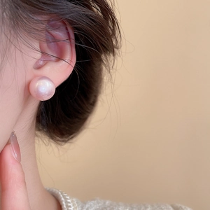 Close-up of elegant round pearl earring with pink iridescent luster worn on the earlobe