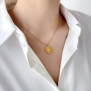 Detail of sun face gold pendant necklace on model wearing a white shirt