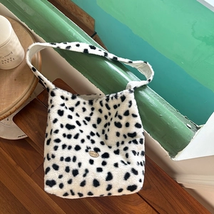 Plush cow print tote bag with soft faux fur texture and a golden metal tag on a wooden step