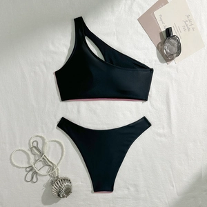 Flat lay of black one-shoulder bikini with pink trim and cutout detail on white fabric