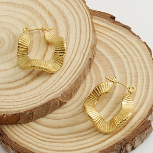 Macro shot of 18K gold plated hoop earrings with irregular wavy texture on wood
