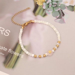 Detail of beaded bracelet with pearl tubes, gold beads and pink stone on floral background
