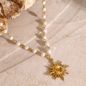 Ciondolo a sole dorato su collana di perle esposta su sfondo in pietra naturale