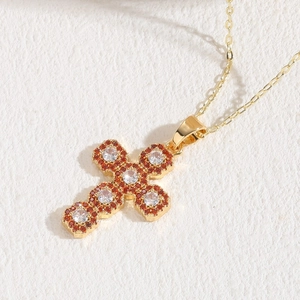 14K gold plated cross pendant necklace with red and white zircons on beige surface