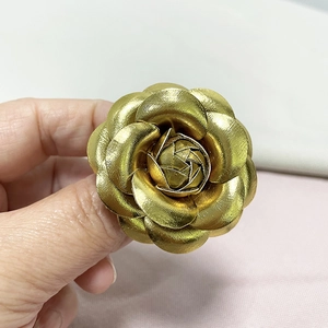 Detail of vintage golden camellia brooch featuring realistic leather texture and metallic petals