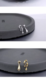 Macro detail of irregular fluid teardrop earrings in polished silver and gold finishes