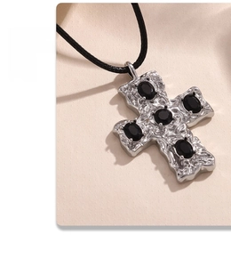 Macro shot of silver cross pendant with hammered texture and oval black stones