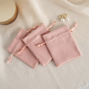 Set of three soft pink velvet drawstring pouches for jewelry storage on textured fabric