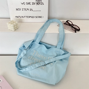 Detail of light blue canvas tote bag featuring white embroidery and adjustable strap