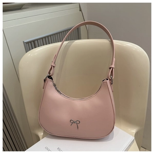 Detailed view of pink crescent shoulder bag with silver bow on a beige chair
