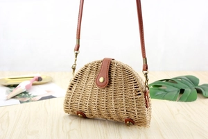 Detail view of the semicircular straw crossbody bag with protective metal feet and brown strap