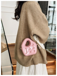 Close-up of pink jelly shoulder bag with metal chain strap worn by a model in a cafe