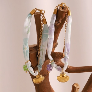 Detail of 18K gold plated seashell charms on floral silk ribbon bracelets on wood