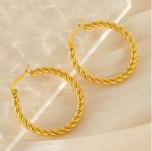 Vue macro de boucles d'oreilles créoles torsadées dorées sur tissu en soie beige