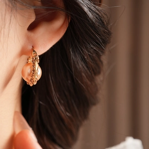 Close-up of a French vintage gold U-shaped earring with pearl and amber crystals on ear
