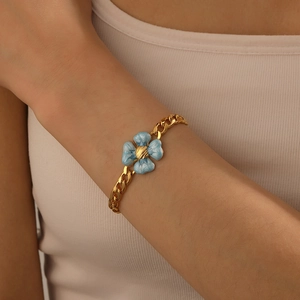 Gros plan d'un bracelet à chaîne dorée avec pendentif fleur bleue au poignet féminin