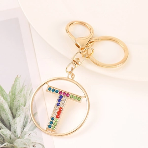 Detail view of golden letter T keychain charm with colorful rhinestones on white plate