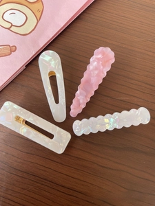 Detailed view of four acetate hair clips in iridescent white and pink on wood surface