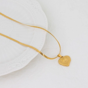 Minimalist gold heart necklace with letter Z engraving on a textured surface