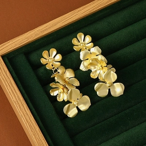 Elegant matte gold layered flower drop earrings on dark green velvet jewelry tray