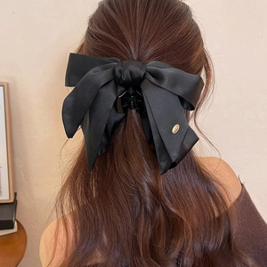 Detail of a black satin bow hair claw clip with a gold metal tag on brown wavy hair