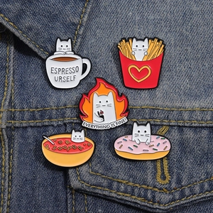 Detail of cute cat enamel pins featuring coffee, fries and donuts on blue denim fabric