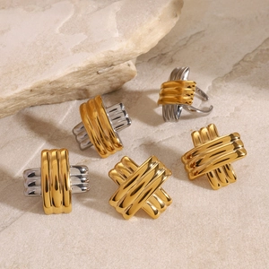 Close-up of X-shaped ribbed earrings and rings in gold and silver steel finishes